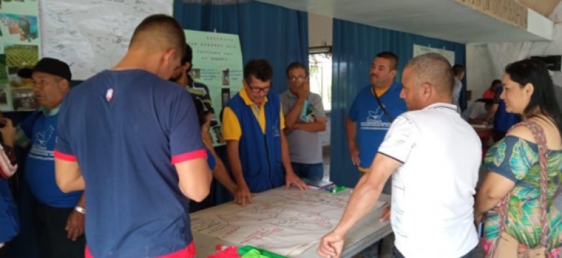 People stand together talking around maps and diagrams on a table